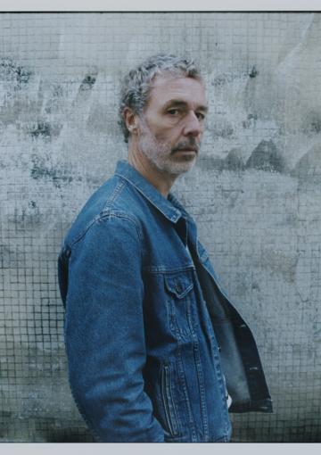Le chanteur Baxter Dury se tient de profil, il porte une veste en jean.